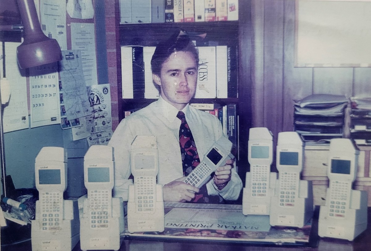 Andrei Spiegel in 1995, behind seven Symbol PDT terminals on a
                    desk, holding an eighth